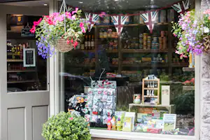 Camping-Shop mit Regalen voller Lebensmittel, davor Deko mit Blumen und Wimpeln in Union-Jack-Optik.