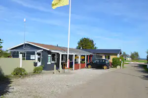 Rezeption am Campingplatz: graues Gebäude mit Eingang, Blumenampeln, Hecken und geparktem Auto an der Zufahrt.
