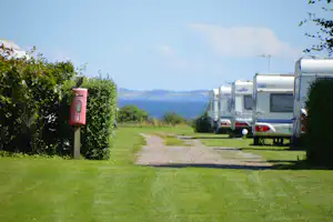 Wohnmobile auf einem Campingplatz, Kiesweg und Rasenfläche, im Hintergrund Berge und grünes Tal.