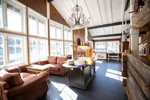 Gemütliche Camping-Lounge mit Ledersofas, Kücheninsel und großen Fenstern, Holzdecke und Kronleuchter im Innenbereich.