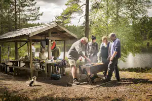 Nordic Camping Hökensås - Camper beim Grillen am überdachten Picknicktisch und See vom Campingplatz