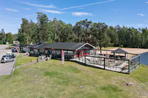 Campingplatz mit Wohnwagen und Stellplätzen, überdachter Terrasse und Grillbereich, umgeben von Bäumen und Rasenfläche.