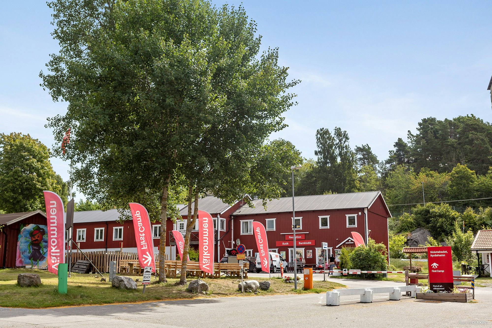 Rote Ferienhaus-Reihe auf einem Campingplatz, mit Sitzbereich, Flaggen und Bäumen im Hintergrund.