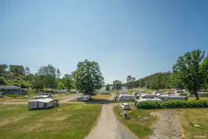 Campingplatz mit Wohnwagen und Stellplätzen, breitem Schotterweg, Rasenflächen und Bäumen entlang der Anlage.