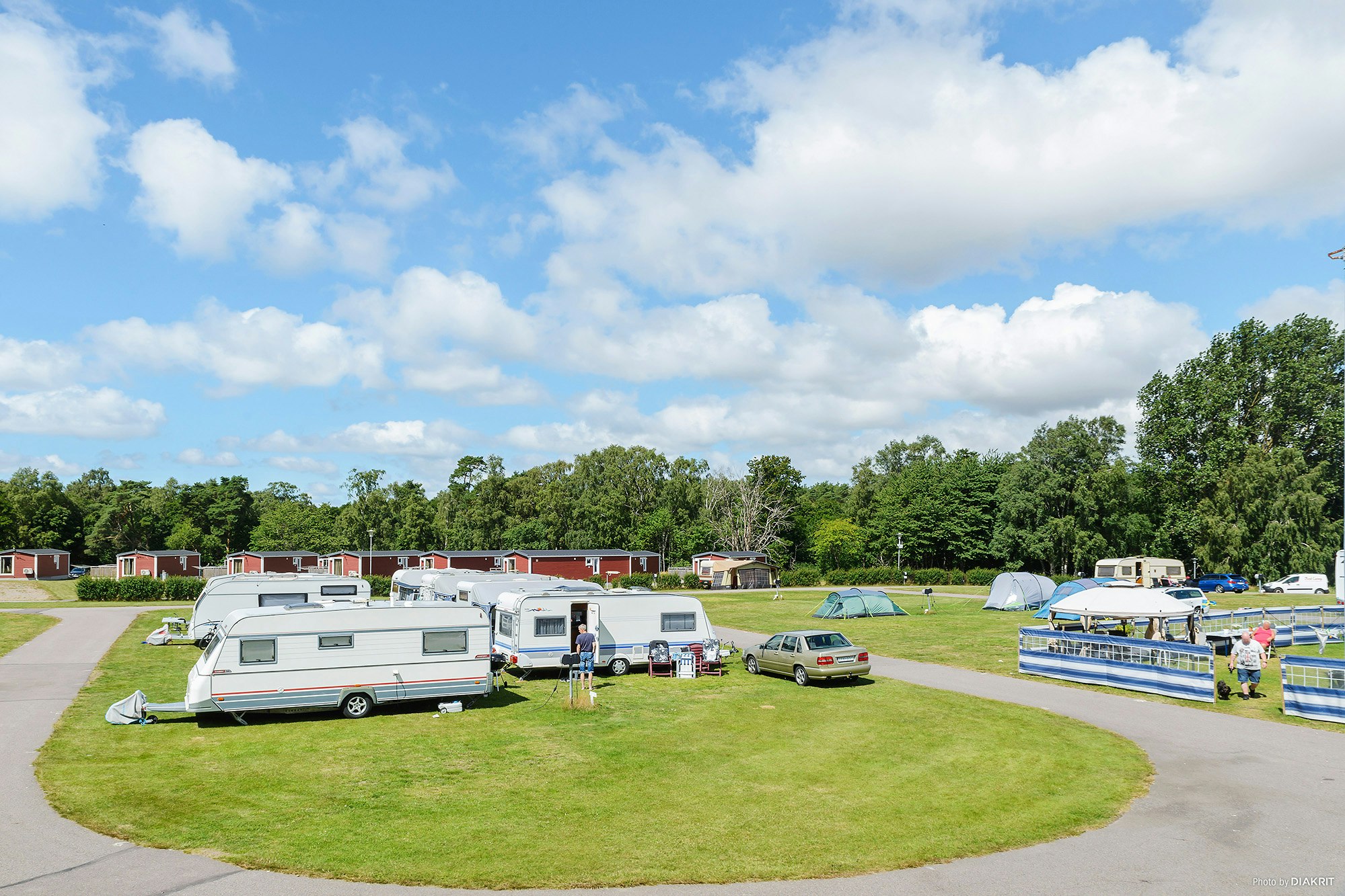 Wohnwagen und Wohnmobile auf einem Campingplatz, mit Rasenflächen, Wegen und mehreren Stellplätzen zwischen Bäumen.