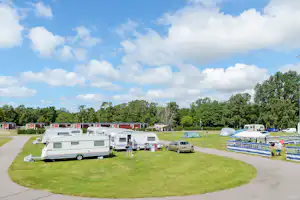 Wohnwagen und Wohnmobile auf einem Campingplatz, mit Rasenflächen, Wegen und mehreren Stellplätzen zwischen Bäumen.