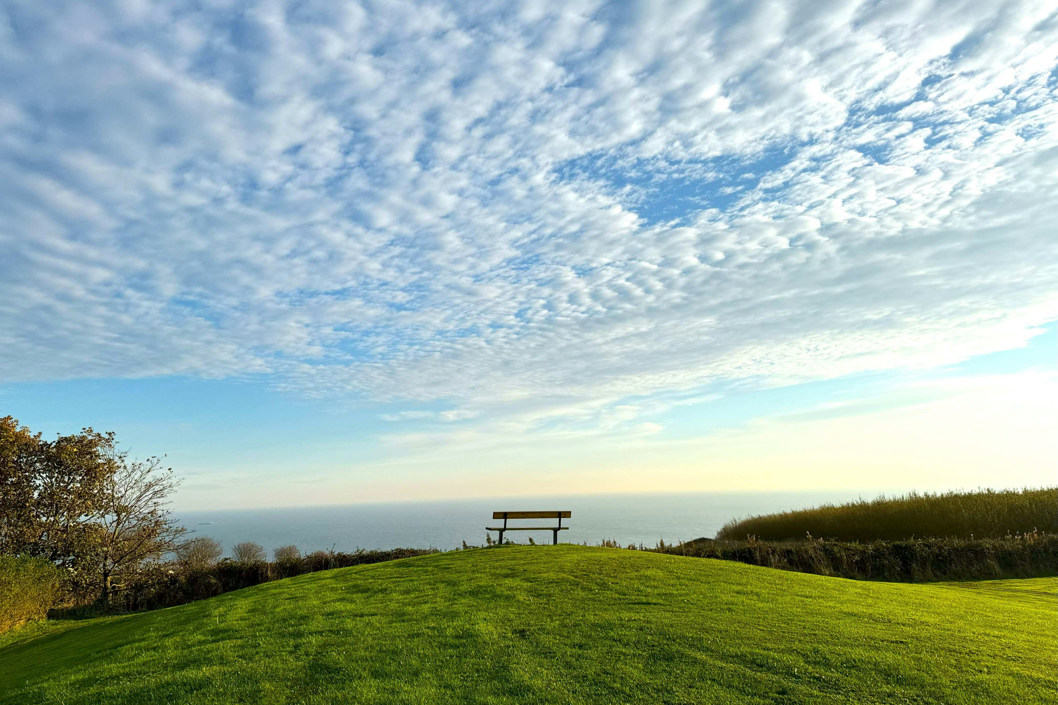 Grüner Hügel mit Aussichtspunkt auf dem Campinggelände, im Hintergrund Wiesen, Bäume und der weite Horizont.