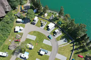 Luftaufnahme eines Campingplatzes am See mit Stellplätzen, kleinen Wohnwagen und Zelten, Wegen und Bäumen am Ufer.