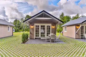 Holzhaus mit Veranda und Sitzplatz, davor ein gepflegter Rasen mit Zierbeeten, daneben weitere Ferienhäuser im Campingbereich.