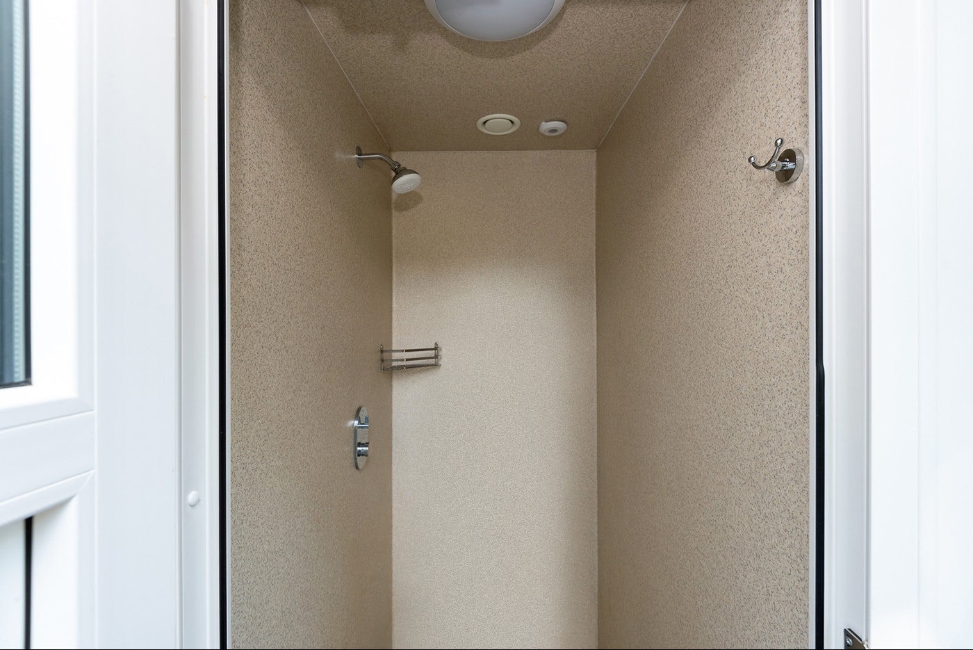 Duschbereich im Camping-Badezimmer mit Duschkopf, Wandarmaturen und beigem Fliesenbereich, sichtbar durch eine offene Tür.