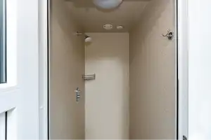 Duschbereich im Camping-Badezimmer mit Duschkopf, Wandarmaturen und beigem Fliesenbereich, sichtbar durch eine offene Tür.