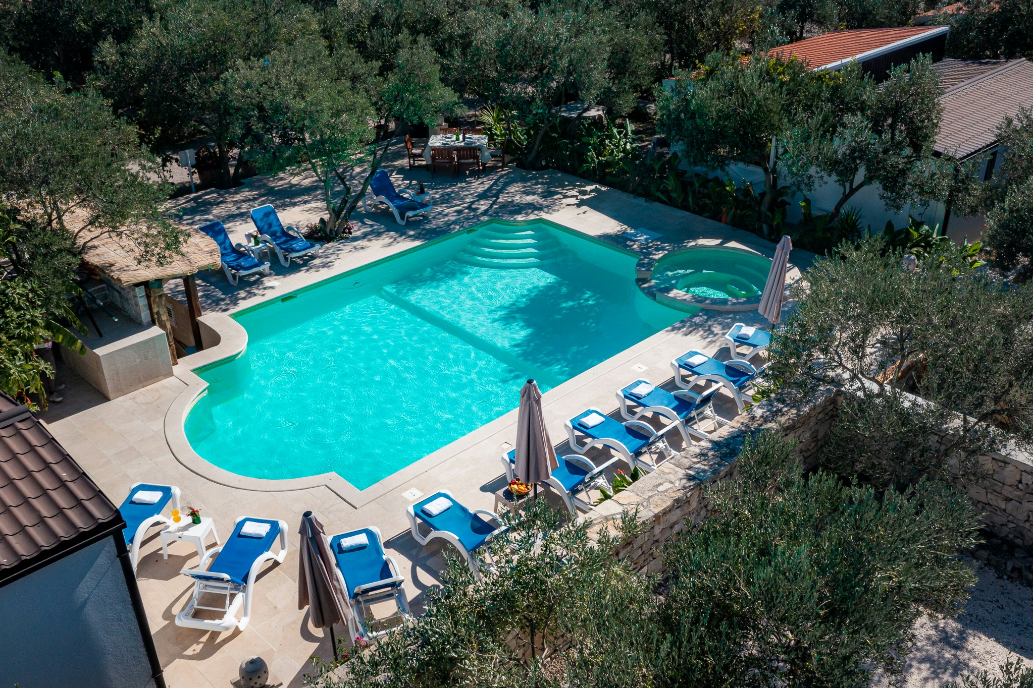 Großes türkisfarbenes Schwimmbecken mit Liegestühlen und Sonnenschirmen, umgeben von Bäumen und einem gepflasterten Bereich am Campingplatz.
