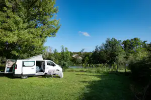 Wohnmobil mit Vorzelt und Campingstuhl auf einer grünen Wiese, umgeben von Bäumen und Hecken.