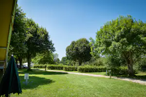 Campingplatz mit Rasenfläche, Baumallee und Kiesweg, im Vordergrund ein Zeltvorzelt und ein Stellplatzschild mit der Nummer 10.