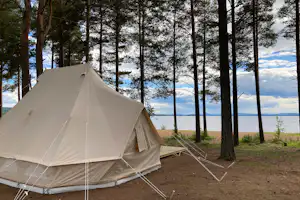 Zelt auf einem Campingplatz am Waldrand, mit Seeblick durch die Bäume und einem Weg am Boden.