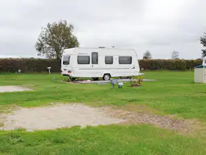 Weißes Wohnmobil auf einem Campingplatz auf grünem Rasen, mit Stellfläche und Hecke im Hintergrund.