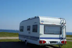 Wohnmobil auf einem Campingplatz am Meer, mit Blick auf die Küste und den Strandweg.