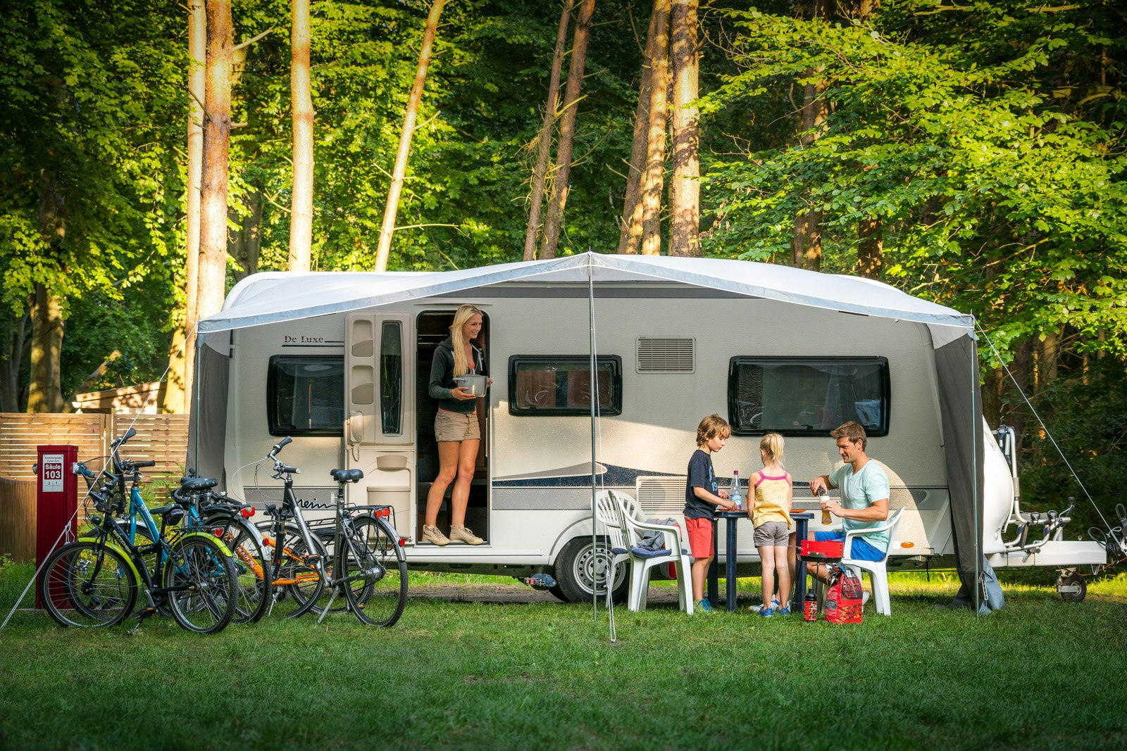 Ostseecamp Rostocker Heide - Familie unter dem Vordach eines Wohnwagens am Wald auf dem Campingplatz