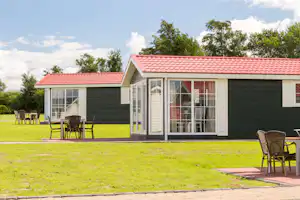 Ostseecamping Familie Heide - auf einer Wiese gelegene, moderne Mietunterkünfte mit großer Fensterfront und einer gepflasterten Terrasse mit Stühlen und einem Tisch