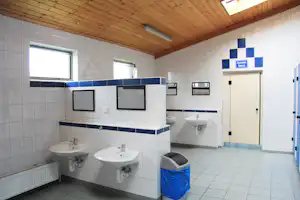 Camping-Badezimmer mit Waschbecken, Spiegeln und Duschbereich, Fliesenboden und beleuchteten Schildern an der Wand.