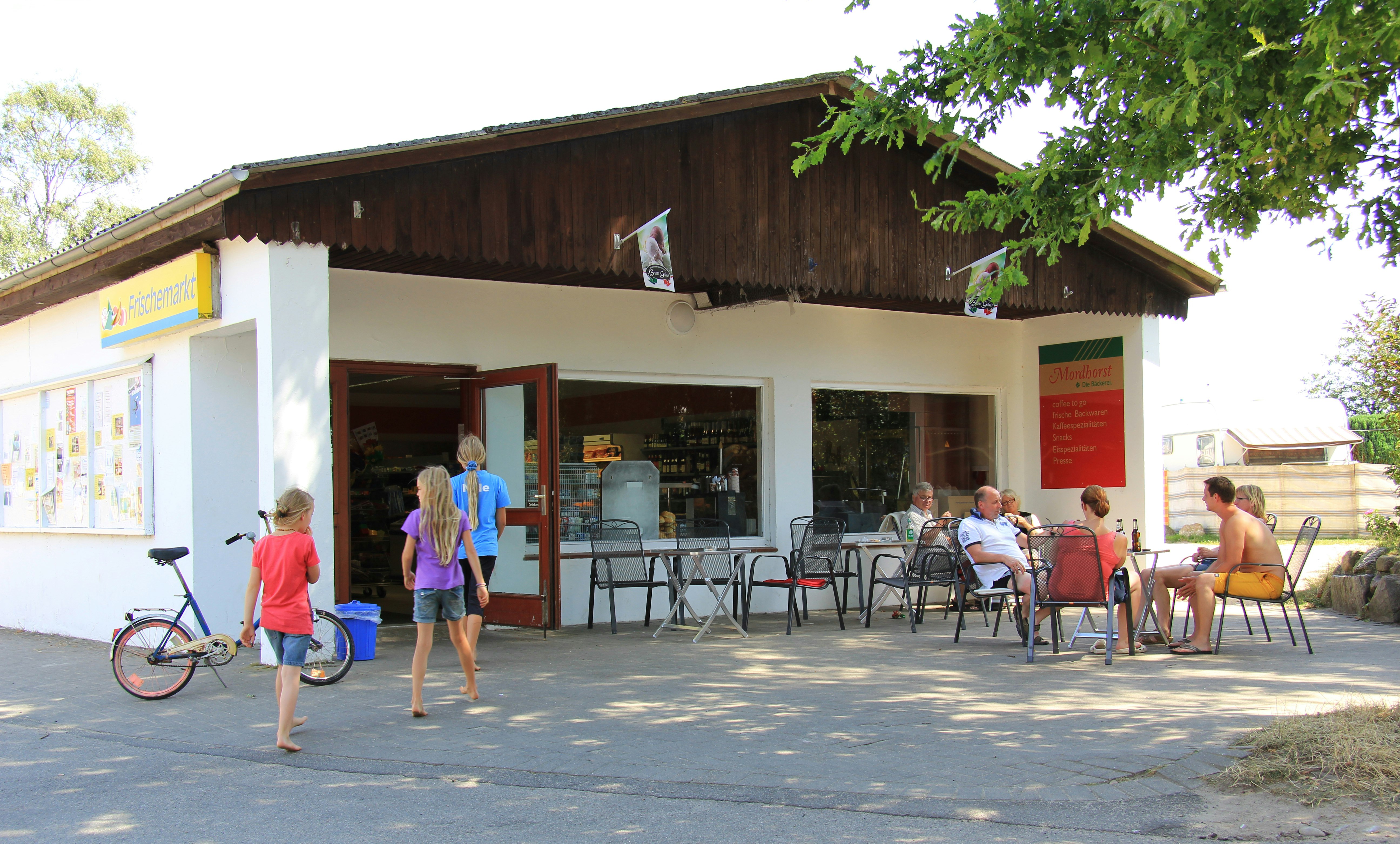 Ostseecamping Gut Karlsminde - Supermarkt mit Terrasse und Stühlen auf dem Campingplatz