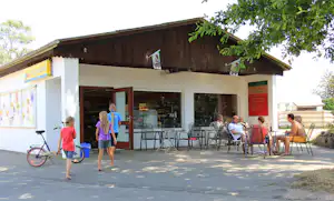 Terrasse am Camping-Restaurant mit Stühlen und Tischen, daneben ein Fahrrad vor dem Gebäude und Menschen im Außenbereich.