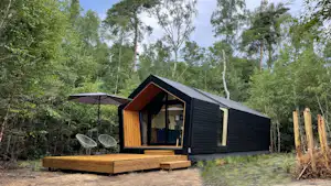 Modernes Holzhaus auf einer erhöhten Plattform mit Terrasse und Markise, umgeben von Bäumen im Campingbereich.