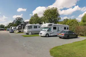 Wohnmobile auf einem Campingplatz-Stellplatz, asphaltierter Weg und Rasenstreifen neben geparkten Fahrzeugen.