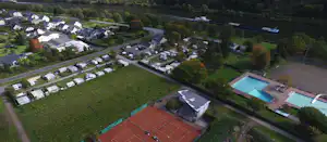 Campingplatz mit Wohnwagen und Stellplätzen, Tennisplatz und Schwimmbecken, umgeben von Feldern und Bäumen, Luftaufnahme.