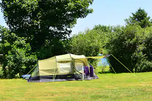 Campingzelt auf einer grünen Wiese mit Vorzelt, daneben ein weiterer Zeltbereich und Bäume im Hintergrund.
