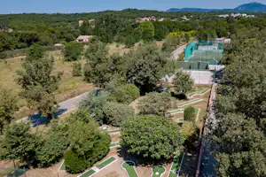 Minigolfanlage mit grünen Bahnen, Wegen und Bäumen auf dem Campinggelände, im Hintergrund weitere Gebäude und Hügel.