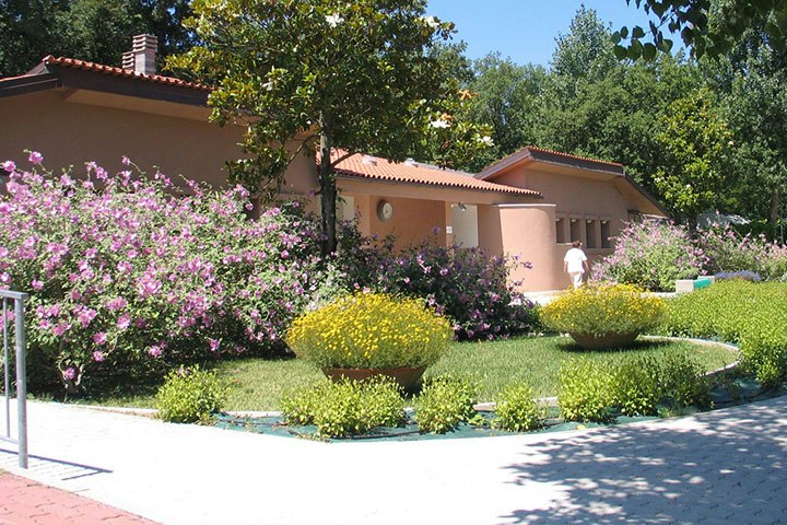 Campinghaus mit roten Ziegeldächern, gepflegtem Rasen und bunten Blumenbeeten vor dem Gebäude im Grünen.