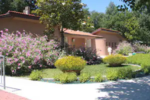 Campinghaus mit roten Ziegeldächern, gepflegtem Rasen und bunten Blumenbeeten vor dem Gebäude im Grünen.