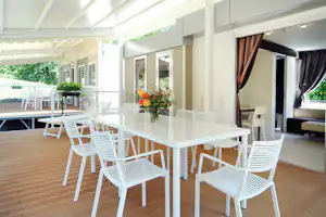 Weiße Terrassenmöbel mit Tisch und Stühlen unter Markisen, Blumenstrauß auf dem Tisch, Blick auf die offene Unterkunft.