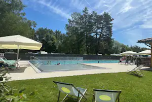 Schwimmbecken auf dem Campingplatz mit Sonnenschirmen, Liegestühlen und Blick auf Bäume und Wohnwagen im Hintergrund.