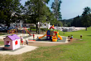 Bunter Spielplatz auf dem Campingplatz mit Rutsche, Klettergerüst und Spielhaus, im Hintergrund Wohnwagen und Bäume.