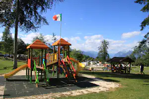 Bunter Spielplatz am Campingplatz mit Rutsche, Pavillon und Blick auf Berge, umgeben von Bäumen und Wohnmobilen.