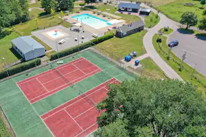 Campinganlage mit großem Schwimmbecken, Tennisplätzen, mehreren Gebäuden, Terrasse und Wegen im grünen Gelände.