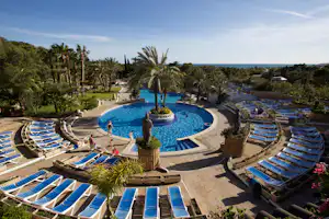 Camping-Pool mit rundem Becken, Palmen und vielen Sonnenliegen, Gartenweg und Blick auf das Meer im Hintergrund.