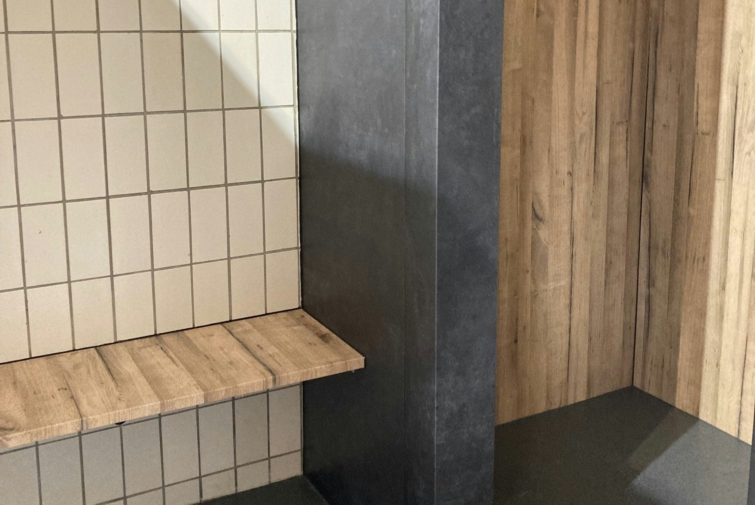 Duschbereich mit gefliesten Wänden, Holzverkleidung und grauem Boden, seitlich eine Armatur an der Wand.