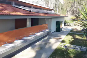 Reihe Waschbecken in einer überdachten Sanitäranlage mit Fliesenwand, Betonablage und Gehweg im Garten.