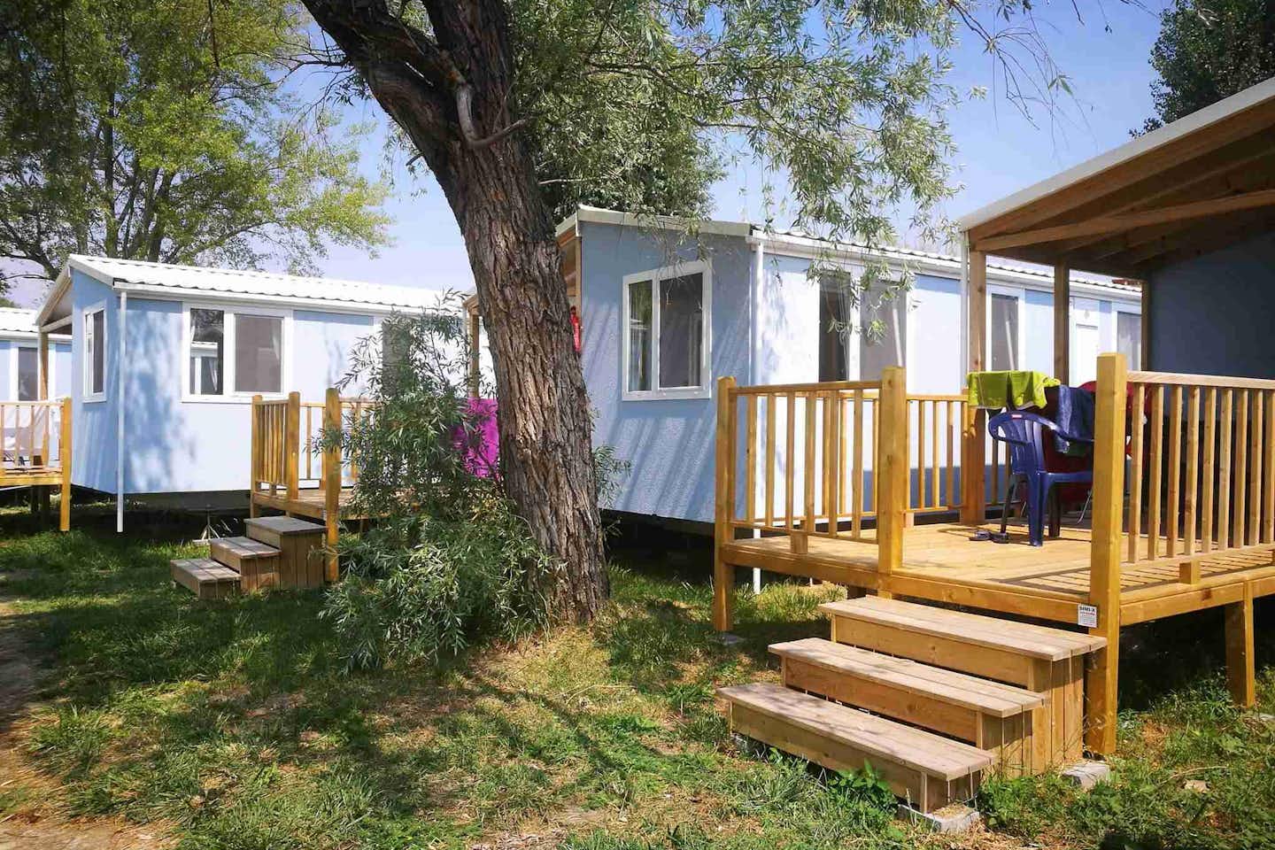 Pelso Camping - Mobilheime mit Veranda und Sitzgelegenheiten zwischen Bäumen