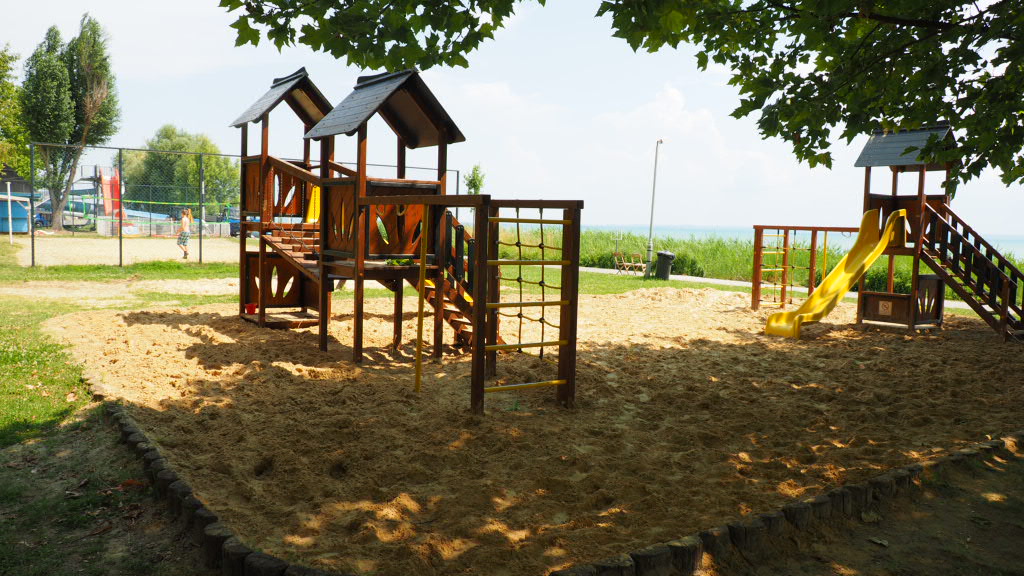Spielplatz mit Klettergerüst und Holzpodesten auf einem Campingplatz, im Hintergrund Bäume und Wiese.