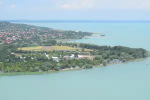 Blick von oben auf eine Küstenlandschaft mit Hafen, Uferpromenade, Häusern und grünen Hängen am Wasser.