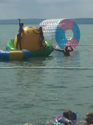 Aufblasbares Wasser-Spiel mit buntem Ballon auf einem Schlauchboot im See, im Hintergrund Wasser und Uferlinie.