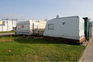 Wohnwagen auf einem Campingplatz-Stellplatz, mit weiteren Caravans und einem Weg zwischen den Parzellen im Hintergrund.