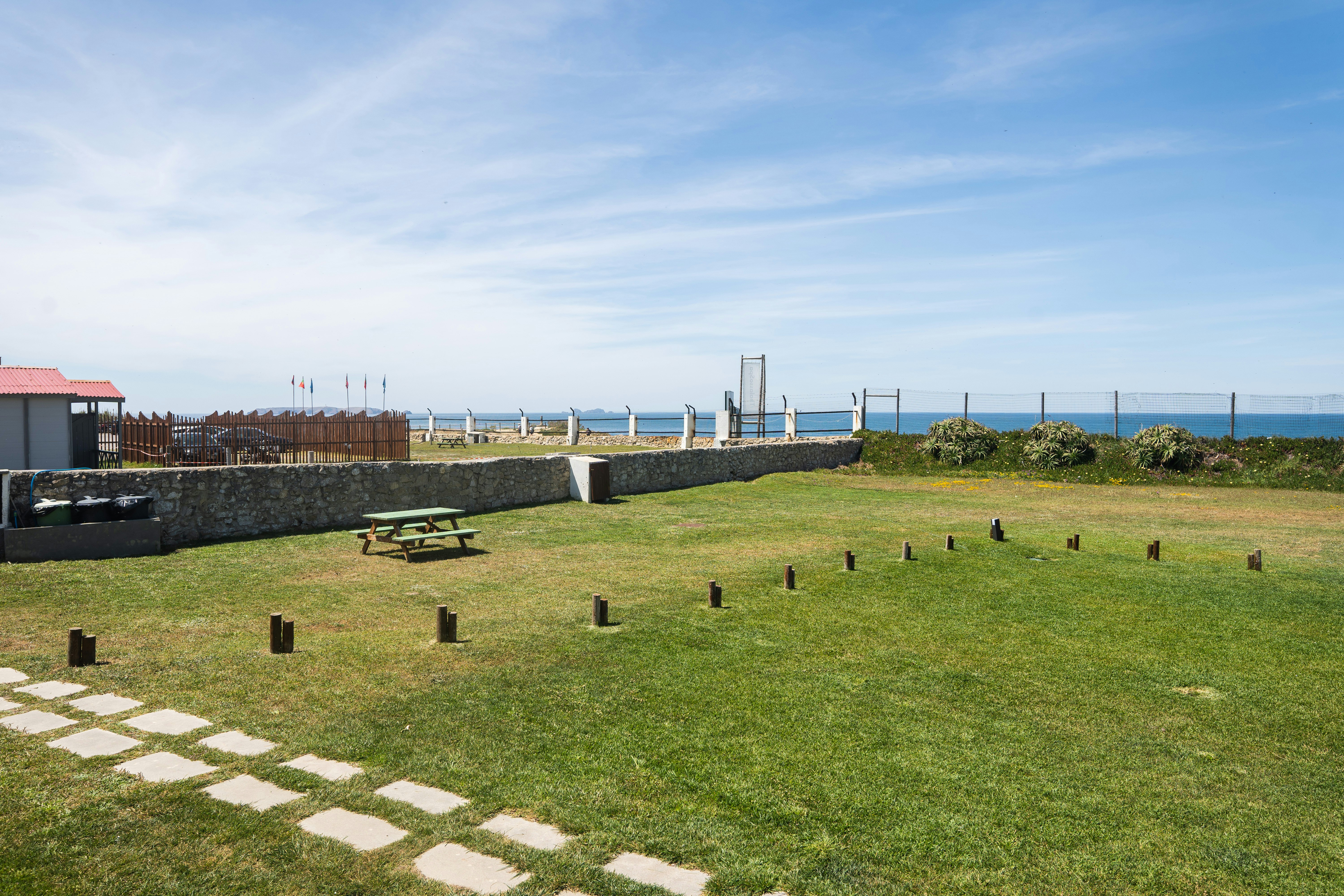 Rasenfläche mit Picknicktisch und niedrigen Holzpfosten, Blick auf das Meer und einen Zaun am Campingplatz.