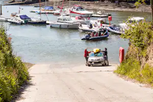 Bootshafen am Campingplatz: mehrere Motorboote und Segelboote im Wasser, daneben ein Auto auf dem Weg.