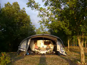 Campingzelt mit offener Vorderseite, Tisch und Stühlen im Inneren, umgeben von Bäumen und Rasen im Grünen.