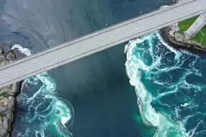 Eine Brücke über einem türkisfarbenen Fluss mit stark schäumenden Stromschnellen und Felsufer.